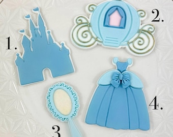 May include: Four blue and white sugar cookies decorated with royal blue icing. The cookies are shaped like a castle, a carriage, a dress, and a mirror. The cookies are numbered 1 through 4.