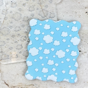 Pode incluir: Dois stencils de plástico transparente, um com um padrão de nuvens e o outro com um padrão de nuvens em um fundo azul claro.