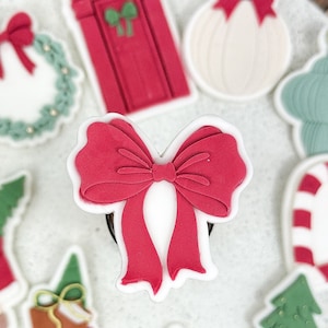 Könnte beinhalten: Ein weißer Teller mit verschiedenen weihnachtlichen Ausstechern. Die Ausstecher zeigen einen Weihnachtsmann, einen Weihnachtsbaum, einen Kranz, eine Schleife, einen Zuckerstock, eine Tür, einen Zweig mit Stechpalme und einen Weihnachtsbaumschmuck.