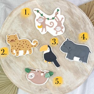 May include: A wooden board with five colorful animal illustrations. The animals are a toucan, a sloth, a hippopotamus, a jaguar, and two monkeys hanging from a vine. Each animal is numbered 1 through 5.