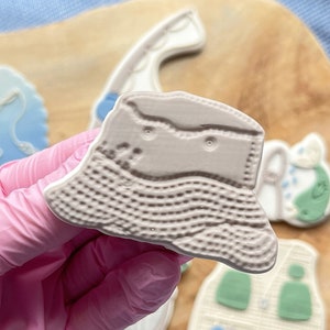 Könnte beinhalten: Ein grauer Plastik-Ausstecher in Form eines Fischerhutes. Der Ausstecher ist mit einem Gittermuster strukturiert und hat ein kleines Loch oben.