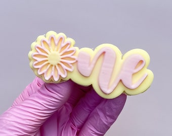 May include: A yellow and pink cookie with the word "one" in pink lettering and a pink flower design.