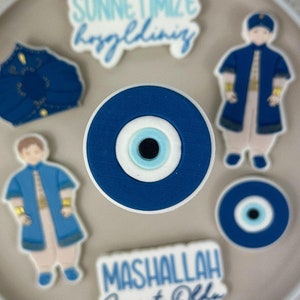 May include: A plate with blue and white decorated cookies. The cookies feature a blue eye design, a phrase in Turkish, and a phrase in English that says "Mashallah Sweet Oklah".