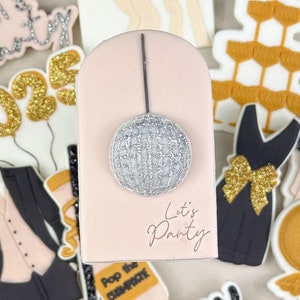 May include: A set of New Year's Eve themed cookie cutters. The cutters are in the shape of a tuxedo, a champagne bottle, a disco ball, a pair of legs, a champagne tower, a dress, a balloon, and a banner that says "Happy New Year".