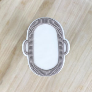 Op de afbeelding: Een witte koek in de vorm van een badkuip met een bruine omtrek. De koek ligt op een houten oppervlak.