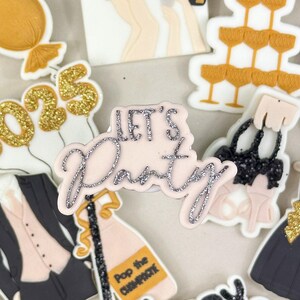 May include: A selection of New Year's Eve decorations on a white plate. Includes a gold balloon, the number 2025, a tuxedo, champagne bottle, a dress, and the words "Let's Party" and "Happy New Year".