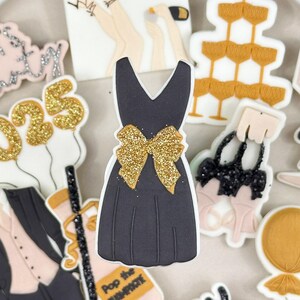 May include: A set of New Year's Eve themed cake toppers featuring a black dress with a gold bow, a tuxedo, a champagne bottle, a glass of champagne, a pair of high heels, a purse, a balloon that says "Happy New Year", and a balloon that says "Let's Party 2025".