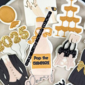 May include: A set of New Year's Eve themed sugar cookies. The cookies are decorated with gold glitter, black icing, and white icing. The cookies include a champagne bottle, a tuxedo, a dress, a champagne glass tower, and balloons that say "2025".