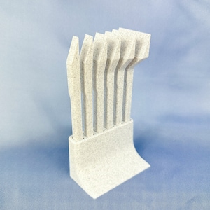 May include: A set of seven white, textured, plastic tools with a curved handle. The tools are arranged in a stand, which is also white and textured.