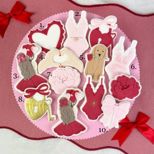 Puede incluir: Una colección de galletas con temática de San Valentín. Las galletas están decoradas con varias formas, incluyendo corazones, lencería, un perro sosteniendo una rosa, una cerradura y llave, y lazos. La paleta de colores incluye rosa, rojo y blanco.