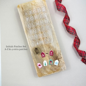 Könnte beinhalten: Ein Holzbrett mit einer transparenten Kunststoffform mit dem Alphabet. Aufnäher mit den Buchstaben A und Z sowie vier zusätzliche festliche Aufnäher sind abgebildet. Ein rot-grünes Karoband ist rechts gewellt.