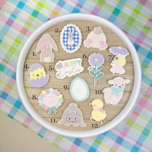 Könnte beinhalten: Eine Sammlung von Verzierungen zum Thema Ostern, darunter ein Hase, ein Küken, ein Lamm und eine Ente. Die Verzierungen sind in Pastellfarben gehalten und weisen verschiedene Designs auf, wie z. B. Blumen, Eier und den Text "Happy Easter".