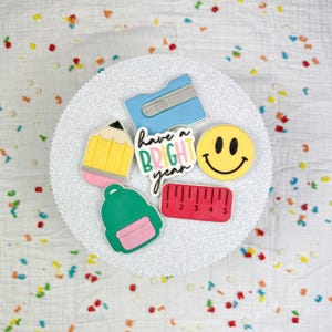 Könnte beinhalten: Eine Sammlung farbenfroher Dekorationen zum Thema Schule, darunter ein gelber Bleistift, ein blauer Spitzer, ein grüner Rucksack, ein rotes Lineal und ein gelbes Smiley-Gesicht. Der Satz "Have a Bright Year" ist ebenfalls enthalten.