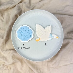 May include: Two PLA stamps on a light blue plate. One stamp is a blue hydrangea flower, and the other is a white goose with a blue bow. The text "1. PLA STAMP" is below the flower stamp.