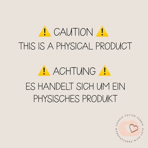 May include: Yellow caution signs with exclamation points and the text "CAUTION THIS IS A PHYSICAL PRODUCT" and "ACHTUNG ES HANDELT SICH UM EIN PHYSISCHES PRODUKT". A pink heart with the text "COOKIE CUTTER FABRIK MANUFACTURED WITH LOVE" in a circle.