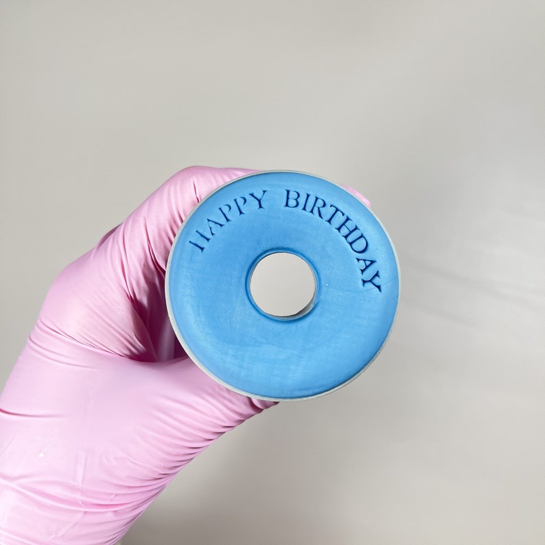 May include: A blue donut-shaped silicone stamp with the words "Happy Birthday" embossed around the edge.