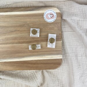 May include: Three cookie cutters on a wooden surface. The cutters are made of metal and have a gold finish. The cutters are shaped like a crescent moon, a star, and a lantern. The text "Mubarak" is printed on the crescent moon cutter.