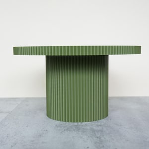 May include: A green, round side table with a ribbed texture. The table has a circular top and a cylindrical base. The table is approximately 20 inches in diameter and 18 inches tall.