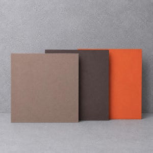 Könnte beinhalten: Drei quadratische Paneele in einer Reihe angeordnet, mit einer glatten, matten Oberfläche. Das erste Paneel ist hellbraun, das zweite dunkelbraun und das dritte leuchtend orange. Jedes Paneel hat gerade Kanten und eine flache Oberfläche.
