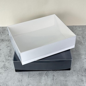 May include: Two-piece gift box set. The top box is white, and the bottom box is black. The boxes are rectangular with a low profile. The boxes are stacked on top of each other. The boxes are empty.