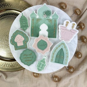 May include: A set of eight green and gold decorated sugar cookies with Islamic designs. The cookies feature an archway, lanterns, and the words "Eid Mubarak" and "Ramadan Kareem".