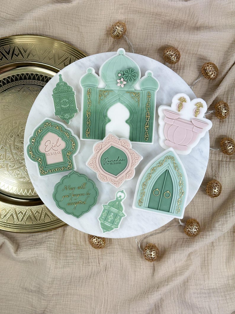 May include: A set of eight green and gold decorated sugar cookies with Islamic designs. The cookies feature an archway, lanterns, and the words "Eid Mubarak" and "Ramadan Kareem".
