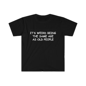 May include: Black t-shirt with white text that reads "IT'S WEIRD BEING THE SAME AGE AS OLD PEOPLE". The shirt is a short-sleeved crew neck style, suitable for casual wear.