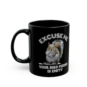 May include: Black ceramic mug with a white squirrel graphic and the text "EXCUSE ME YOUR BIRD FEEDER IS EMPTY". The mug has a curved handle and a glossy finish.