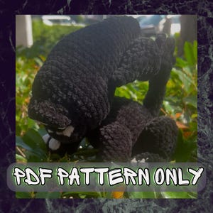 May include: A black crocheted creature with white accents, possibly a cat or a similar animal, is shown in a natural outdoor setting. The text "PDF PATTERN ONLY" is displayed across the bottom of the image.