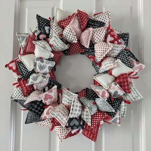 May include: A wreath made of fabric hearts in red, white, and black with a variety of patterns and the words "Love is Love" printed on some of the hearts.