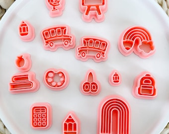 May include: A set of 15 pink plastic cookie cutters shaped like school supplies, including a bus, apple, rainbow, pencil, and calculator.