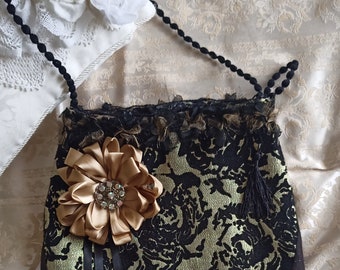 May include: A black and gold fabric handbag with a floral pattern and a large gold satin bow. The bag has a black crocheted trim and a black beaded strap.