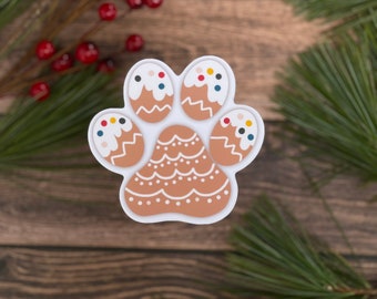 May include: A white gingerbread cookie shaped like a paw print with brown icing and colorful sprinkles. The cookie is decorated with white icing and a zig-zag pattern.