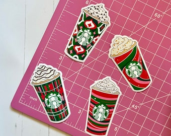Puede incluir: Cuatro pegatinas de vasos de café Starbucks con temática navideña. Las pegatinas presentan un diseño de cuadros rojos y verdes, un diseño de rayas rojas y verdes y un diseño geométrico rojo y verde. Cada pegatina tiene una cobertura de crema batida blanca y un logotipo de Starbucks.