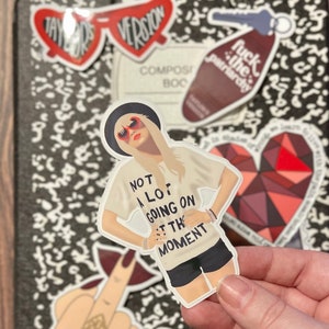 Peut inclure: Un autocollant repr&eacute;sentant une femme aux cheveux blonds portant des lunettes de soleil et un t-shirt blanc avec le texte "Not a lot going on at the moment".