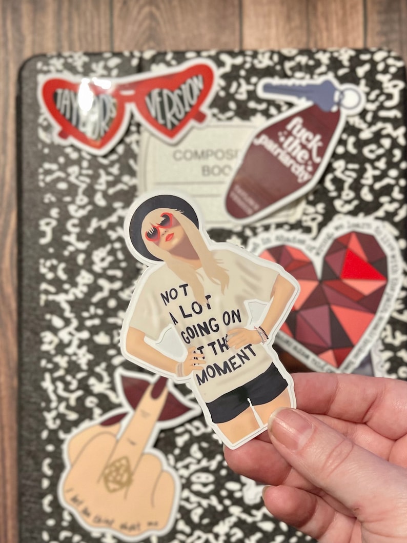 Peut inclure: Un autocollant repr&eacute;sentant une femme aux cheveux blonds portant des lunettes de soleil et un t-shirt blanc avec le texte "Not a lot going on at the moment".