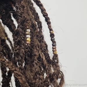 May include: Close-up of brown dreadlocks adorned with metallic beads in gold, silver, and bronze. The locs are tightly twisted, showcasing the texture and style. The beads add a decorative element to the hairstyle.