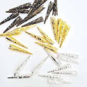 Puede incluir: Una variedad de accesorios decorativos para el cabello en tonos dorados, plateados y bronce. Las joyas metálicas para el cabello presentan intrincados diseños de filigrana y vienen en varias formas y tamaños. La imagen incluye el texto "Bijoux goddess pour petites locks" y una dirección web.