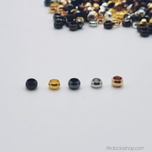 May include: An assortment of metal hair beads in gold, silver, bronze, and black. The cylindrical beads have a central hole, designed for use in dreadlocks or other hair styles. The image also includes the website address Afrolocksshop.com.
