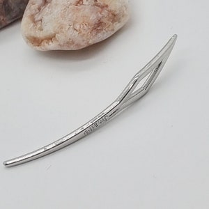 Peut inclure: Une pince à cheveux en argent de forme diamantée. La pince est incurvée et porte une petite inscription au dos qui indique "925 Sterling".