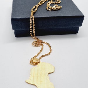 K&ouml;nnte beinhalten: Eine goldene Kettenkette mit einem goldenen Anh&auml;nger in Form des afrikanischen Kontinents. Die Kette liegt auf einer schwarzen Schachtel.
