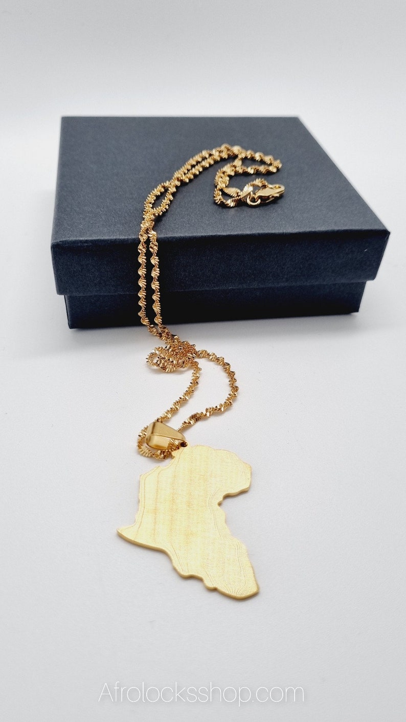 K&ouml;nnte beinhalten: Eine goldene Kettenkette mit einem goldenen Anh&auml;nger in Form des afrikanischen Kontinents. Die Kette liegt auf einer schwarzen Schachtel.
