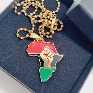 K&ouml;nnte beinhalten: Goldkette mit einem Anh&auml;nger in Form des afrikanischen Kontinents. Der Anh&auml;nger ist rot, schwarz und gr&uuml;n mit einer goldenen Faust, die in die Luft gehoben wird.
