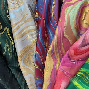 Puede incluir: Una colección de muestras de tela coloridas con un diseño veteado. Las telas presentan detalles metálicos dorados y una variedad de colores, incluyendo verde, blanco, rojo, azul, rosa y naranja. La tela tiene una calidad brillante y reflectante.