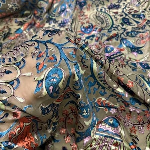 Puede incluir: Primer plano de una tela con un detallado estampado de cachemira. La tela presenta un color base verde oliva con intrincados diseños en tonos azules, naranjas y morados. El patrón incluye elementos florales y curvos.