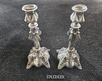 May include: A pair of silver candle holders with ornate designs. The candle holders have a tall, slender base with a decorative top.