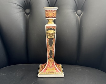 Peut inclure: Un bougeoir décoratif en céramique avec des motifs dorés, rouges et noirs. Il présente un emblème de tête de Méduse dorée et des motifs ornés. La base est carrée et le sommet est conçu pour une bougie.