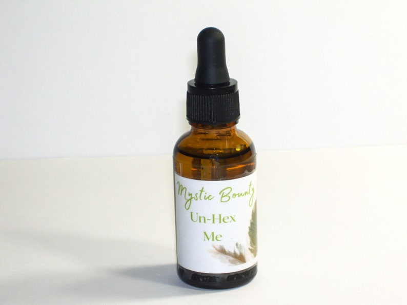 Op de afbeelding: Een bruine glazen fles met een druppelaar en een wit etiket met de tekst "Mystic Bounty Un-Hex Me".