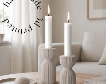 May include: Two lit white candles in beige 3D-printed candle holders. The holders have a ribbed design and sit on a wooden table. The text "handmade 3d-printed" is in a circular arrangement above the candles.