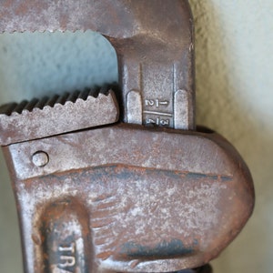 Może przedstawiać: Rdzawy klucz nastawny z srebrnym uchwytem i nadrukiem "TRADE" na boku. Klucz ma skalę pomiarową z oznaczeniami "1-1/4" i "1-1/2".